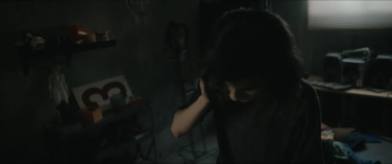 Death to Summer (2021) movie still: medium — A dimly lit bedroom features a shelf with various small objects and a window. A person with dark hair…