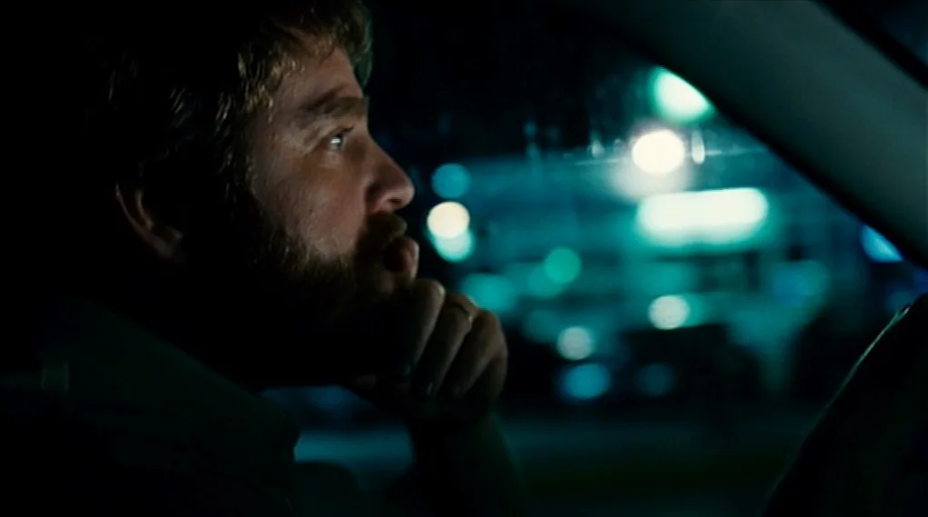 Visioneers (2008) movie still: closeup — The interior of a vehicle at night with blurred city lights in the background. A man sits behind the wheel,…