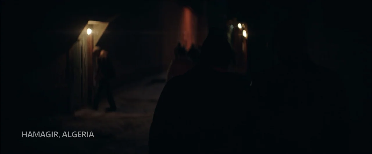 Redemption Day (2021) movie still: wide — A dark, narrow alleyway at night in Hamagir, Algeria with indistinct silhouettes present. Several people…