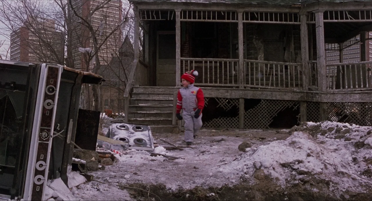 Child’s Play (1988) movie still: fullbody — A young boy walks across a desolate lot littered with debris and patches of snow. An abandoned, decaying…