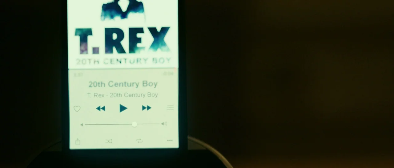 The Purge: Election Year (2016) movie still: closeup — A dimly lit room is centered on a smartphone displaying a music streaming interface. The…
