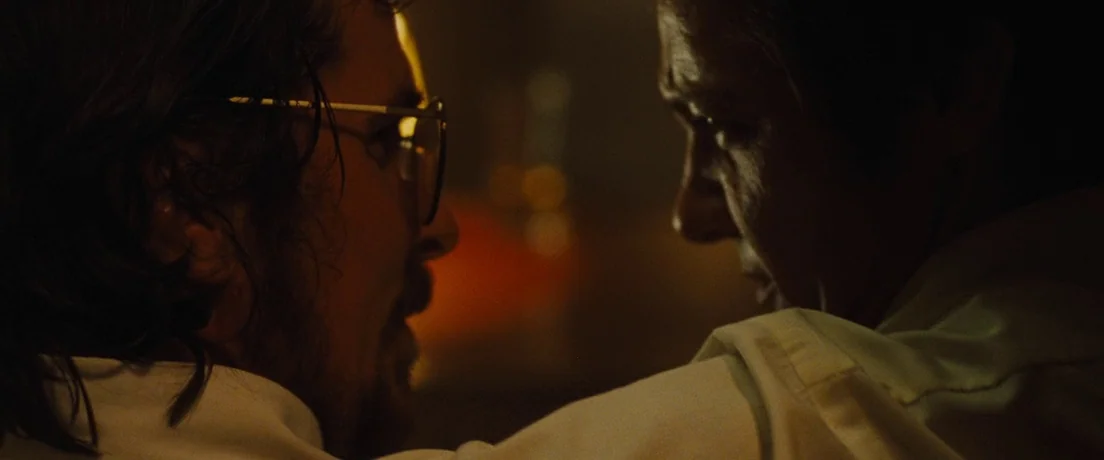 American Hustle (2013) movie still: closeup — Two people face each other in a dimly lit vehicle during the night. The warm light from an unseen…