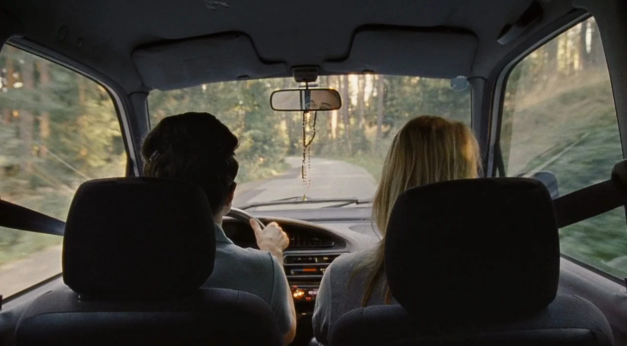 Paradise: Hope (2013) movie still: medium — The interior of a moving vehicle as seen from the backseat perspective. A man and a woman drive along a…