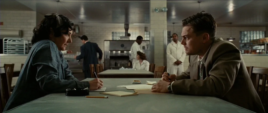 Shutter Island (2010) movie still: medium — A sterile cafeteria with light-colored tile walls and long tables under fluorescent lights. A man in a…