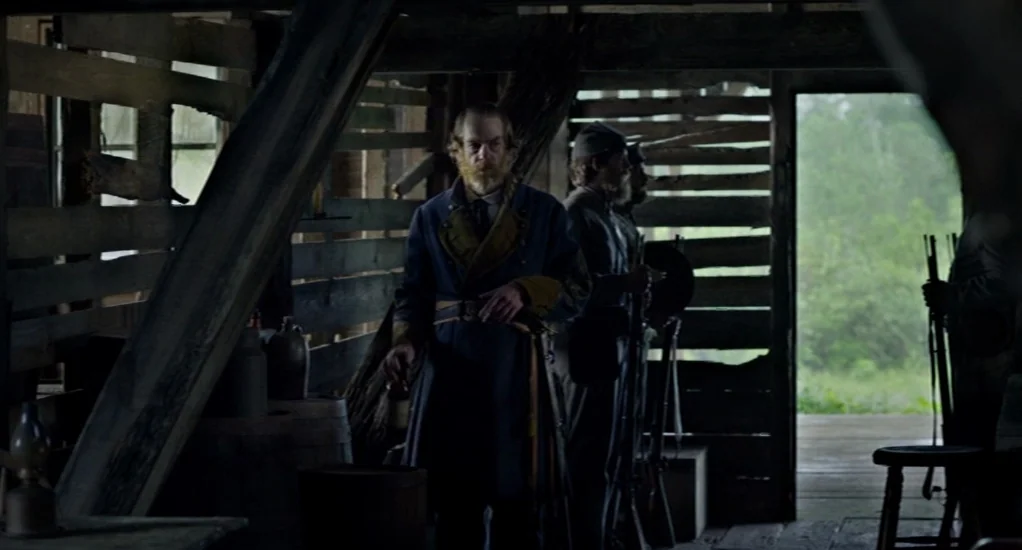 Free State of Jones (2016) movie still: medium — A dimly lit wooden structure with slat walls and a central figure. The man wearing a blue military…
