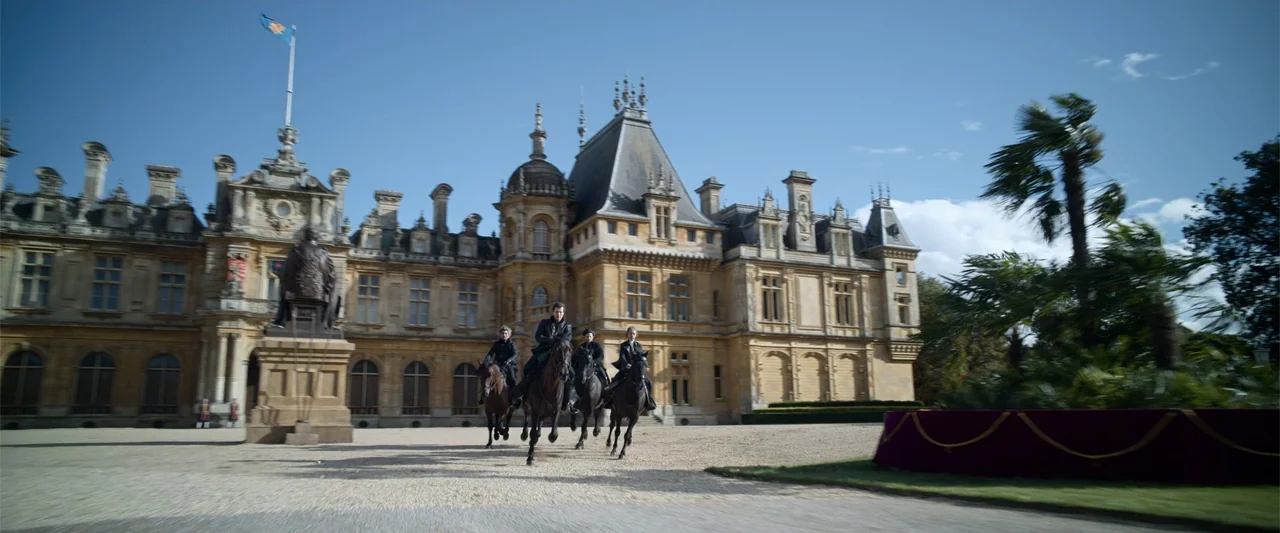 Cinderella (2015) movie still: wide — A large stone mansion with intricate architecture stands behind a paved gravel entrance area. Four riders in…