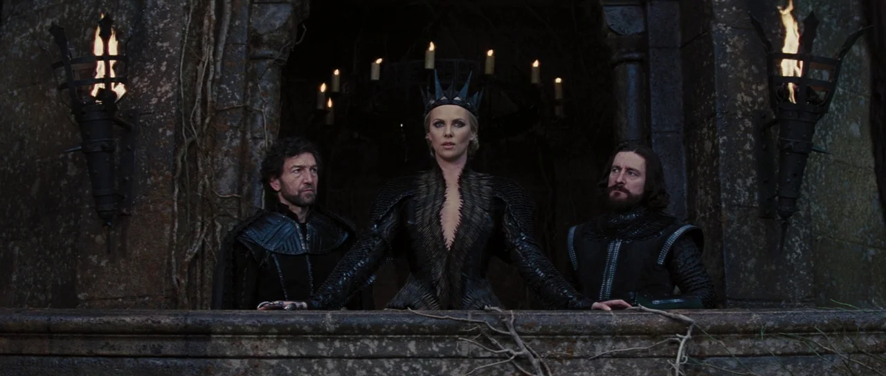 Snow White and The Huntsman (2012) movie still: medium — A stone balcony at night features flickering torches on either side of three figures. A…