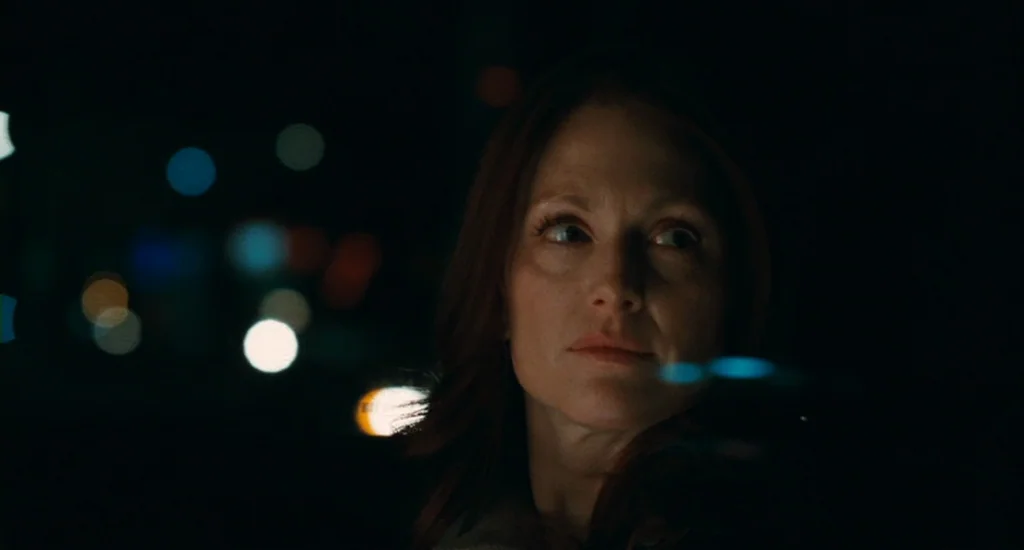 Chloe (2009) movie still: closeup — A woman sits inside a car at night with darkness surrounding her. She looks toward the side window at blurred…