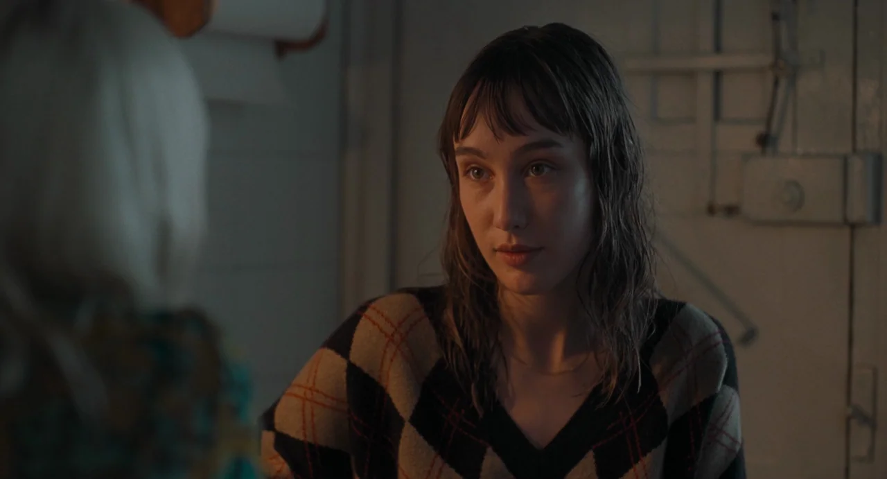 La Abuela (2021) movie still: medium — A dimly lit room with a paneled wall and a mechanical utility switch visible. A young woman with damp hair…