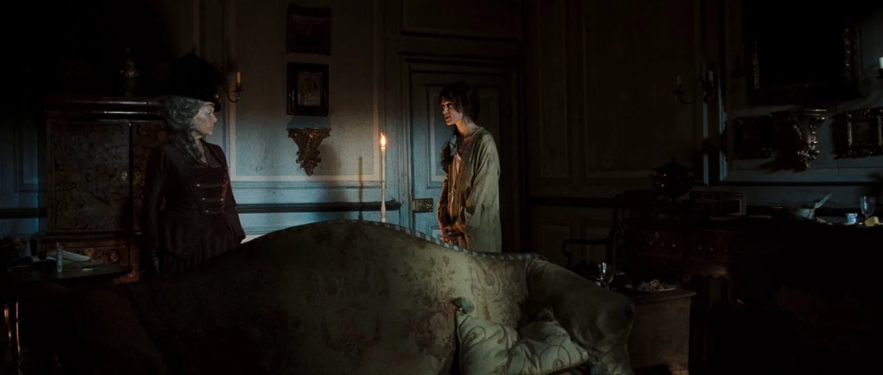 Pride & Prejudice (2005) movie still: wide — A dimly lit 19th-century room with dark wood walls and ornate wall carvings. An older woman and a young…