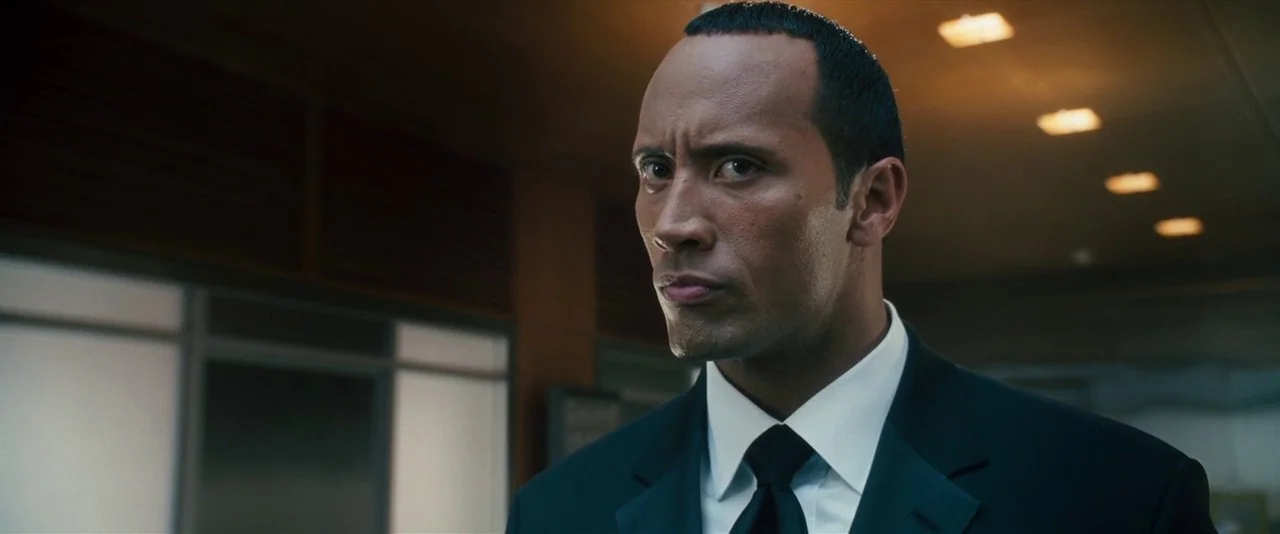 Southland Tales (2006) movie still: closeup — A professional interior office environment featuring drop ceilings with recessed lighting fixtures. A…