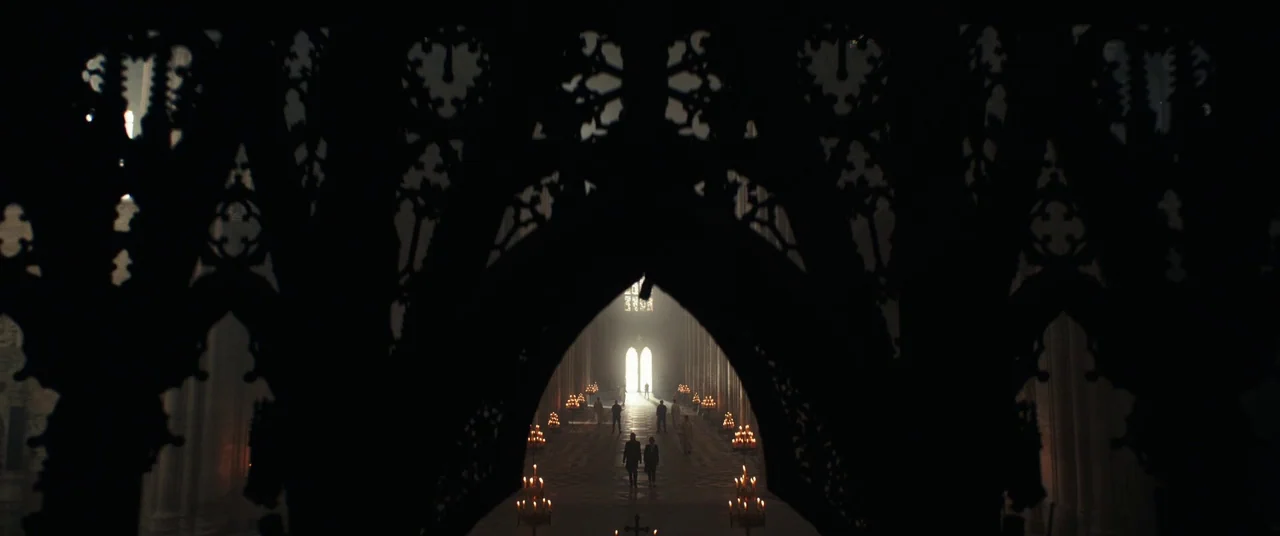 Assassin’s Creed (2016) movie still: establishing — A vast stone cathedral nave with ornate Gothic arches framing a deep perspective view. Multiple…