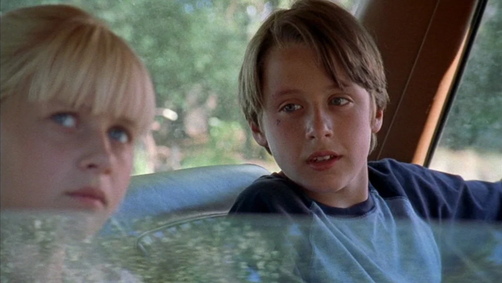 Mean Creek (2004) movie still: medium — A view from inside the backseat of a moving vehicle on a bright day. Two children sit side by side and gaze…