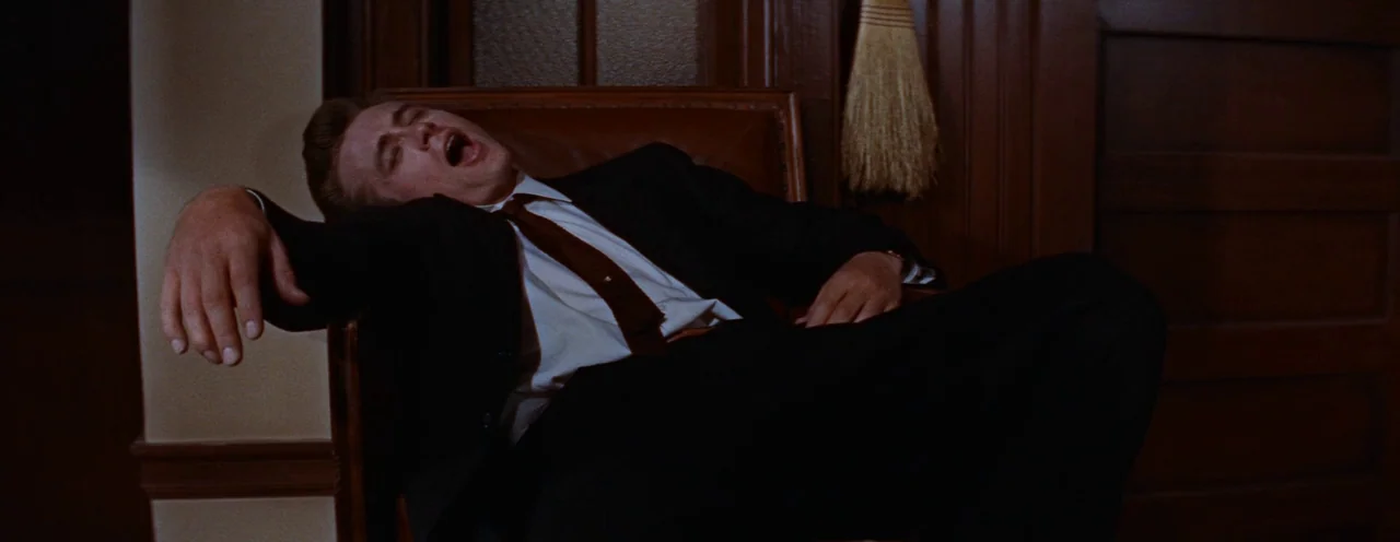 Rebel Without A Cause (1955) movie still: medium — A man in a suit sleeps in a leather chair within a wood-paneled room. The man sits with his head…
