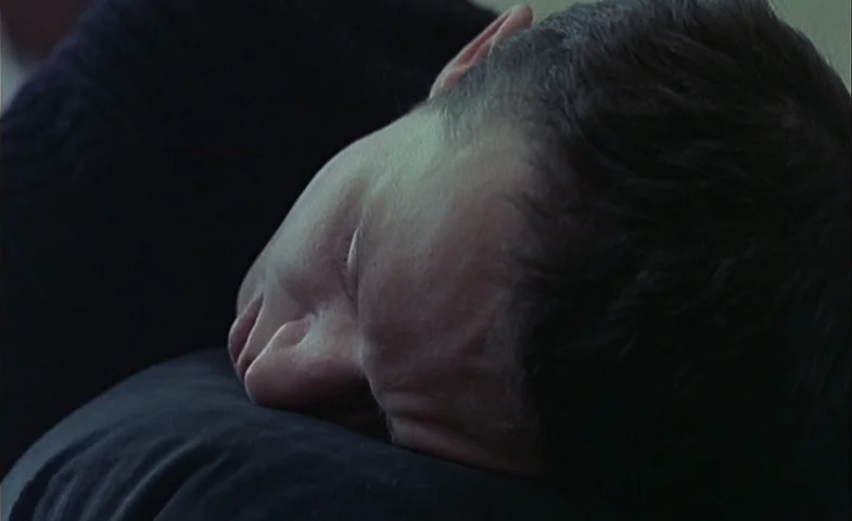 Blind Chance (1987) movie still: closeup — A close view of a person resting their head against a dark-colored pillow. The subject has short hair and…