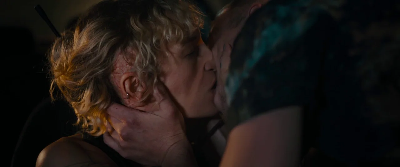 Titane (2021) movie still: closeup — The interior of a dark car at night. A couple embraces and kisses in close proximity.