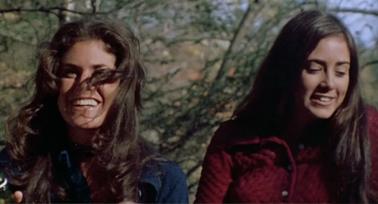 The Last House on the Left (2009) movie still: medium — Two young women with brown hair stand outdoors against a blurry background of trees. They…