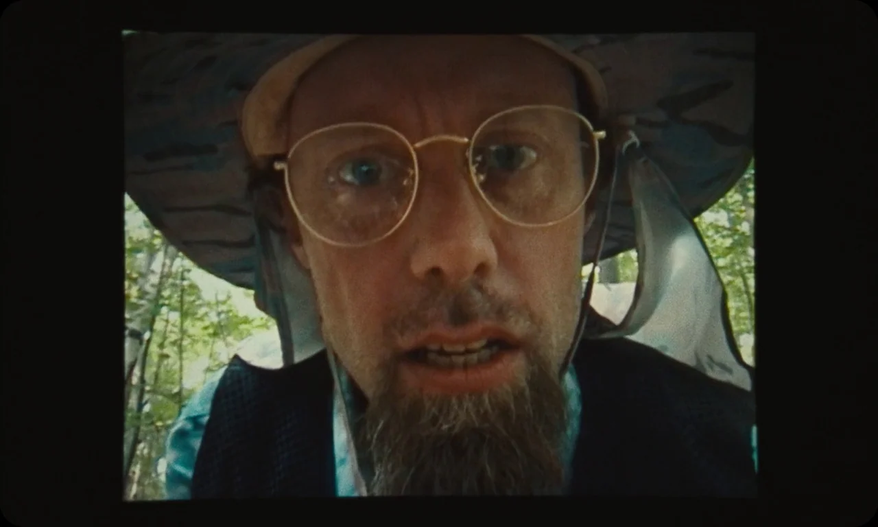 Vulcanizadora (2024) movie still: closeup — A man stands outdoors in a leafy forest environment during the day. He stares directly downward into the…