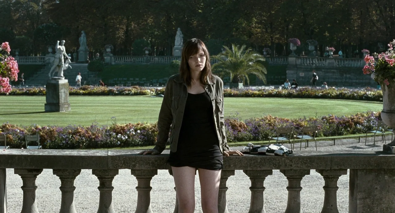 Reprise (2006) movie still: medium — A well-manicured public park features ornate stone statues and a formal lawn background. A young woman rests…