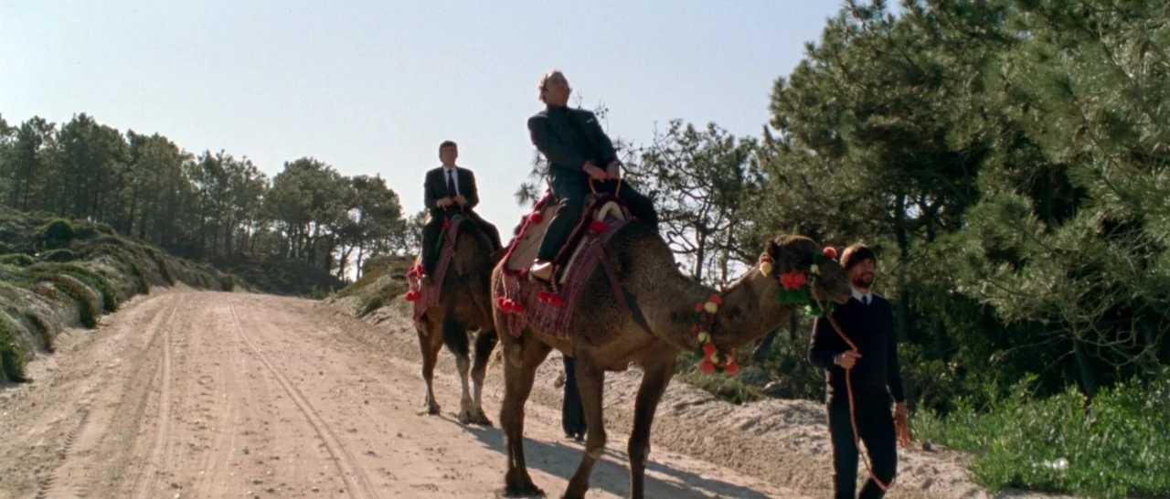 Arabian Nights: Volume 1 – The Restless One (2015) movie still: wide — A wide dirt road winds through a pine-forested area on a clear day. Two men…