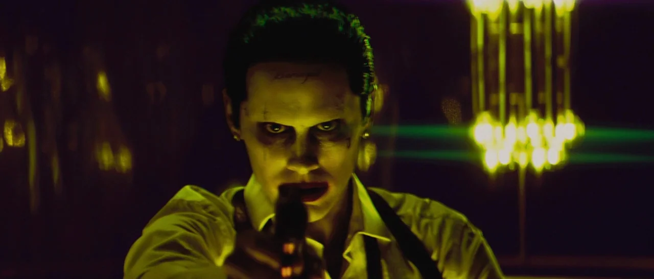 Suicide Squad (2016) movie still: closeup — A dark, dimly lit lounge features glowing decorative lights in the background. A man stares directly at…