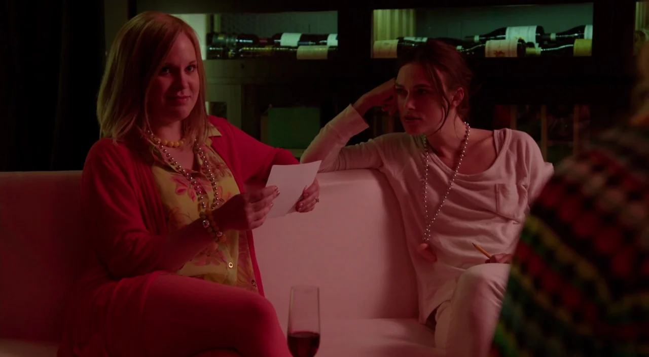 Laggies (2014) movie still: medium — A lounge area with a white sofa situated in front of a wine storage unit. Two women in casual attire converse…