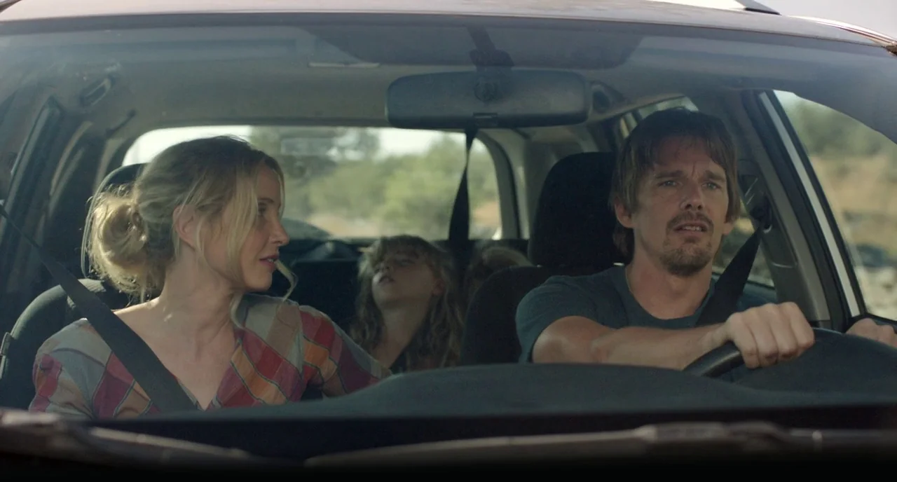 Before Midnight (2013) movie still: medium — A modern car interior with a man driving and a woman in the passenger seat. A young child sleeps in the…