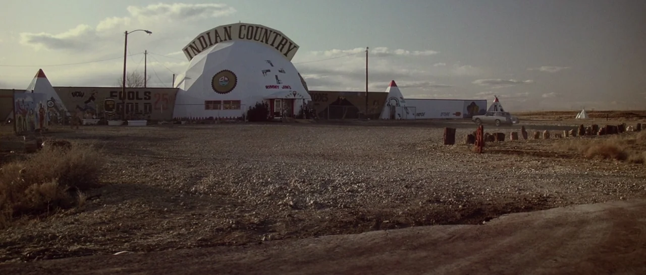 Starman (1984) movie still: wide — A roadside shop features a white geodesic dome with Indian Country signage in desert terrain. A single car sits…