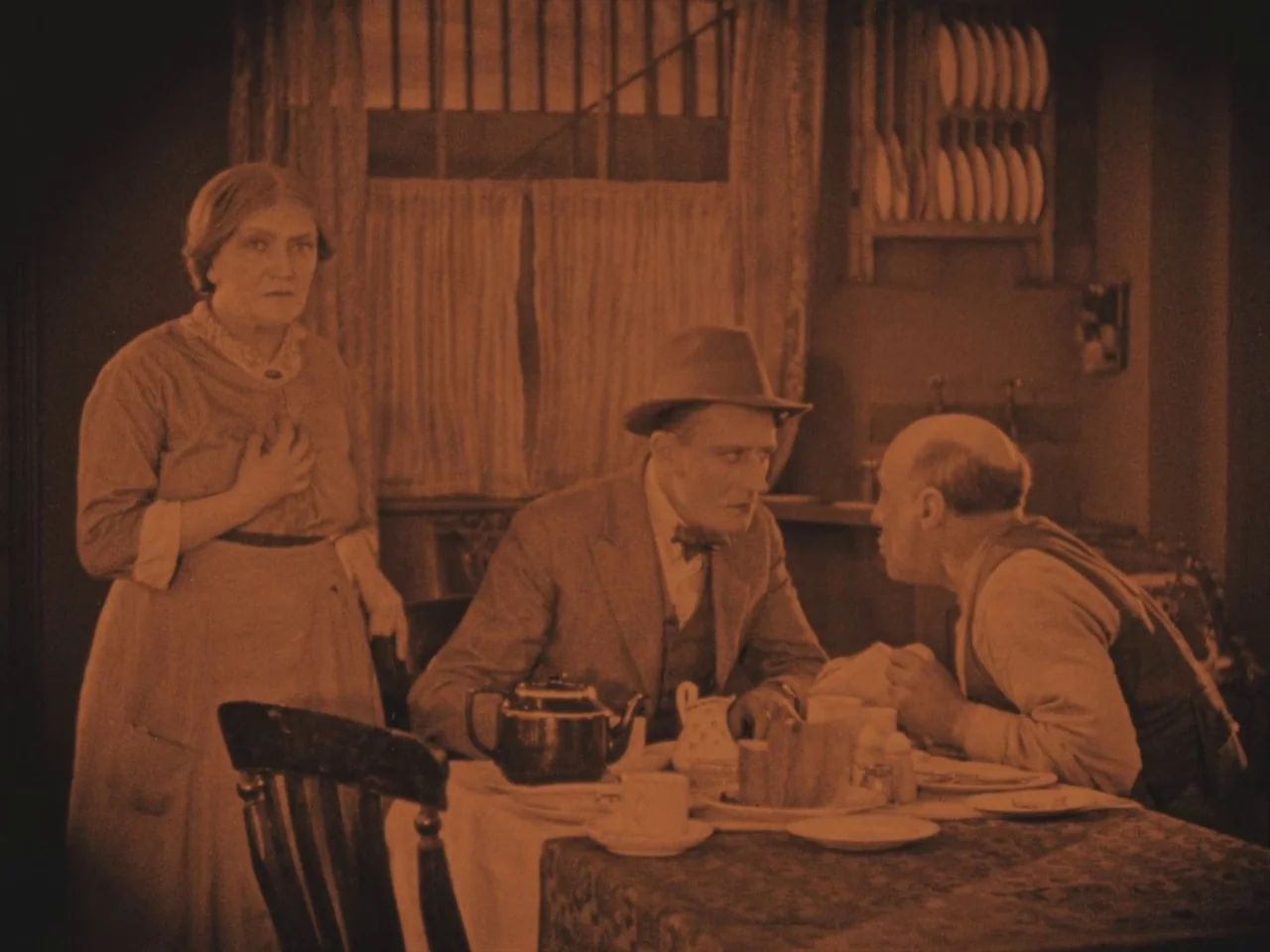 The Lodger (1927) movie still: medium — A modest dining room features a set table with a tea service and plates. A woman stands beside a man in a…