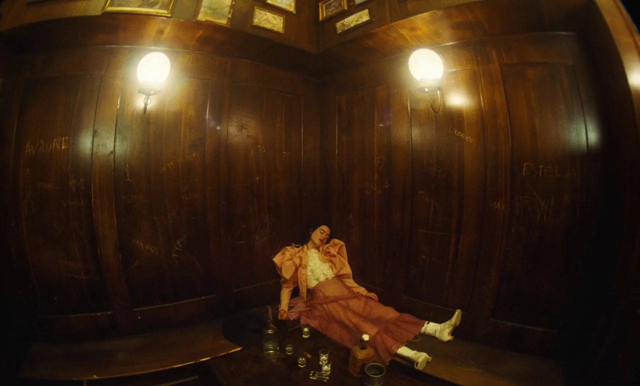 Poor Things (2023) movie still: wide — A dark corner with floor-to-ceiling wood paneling features graffiti etched into the wood surfaces. A woman in…
