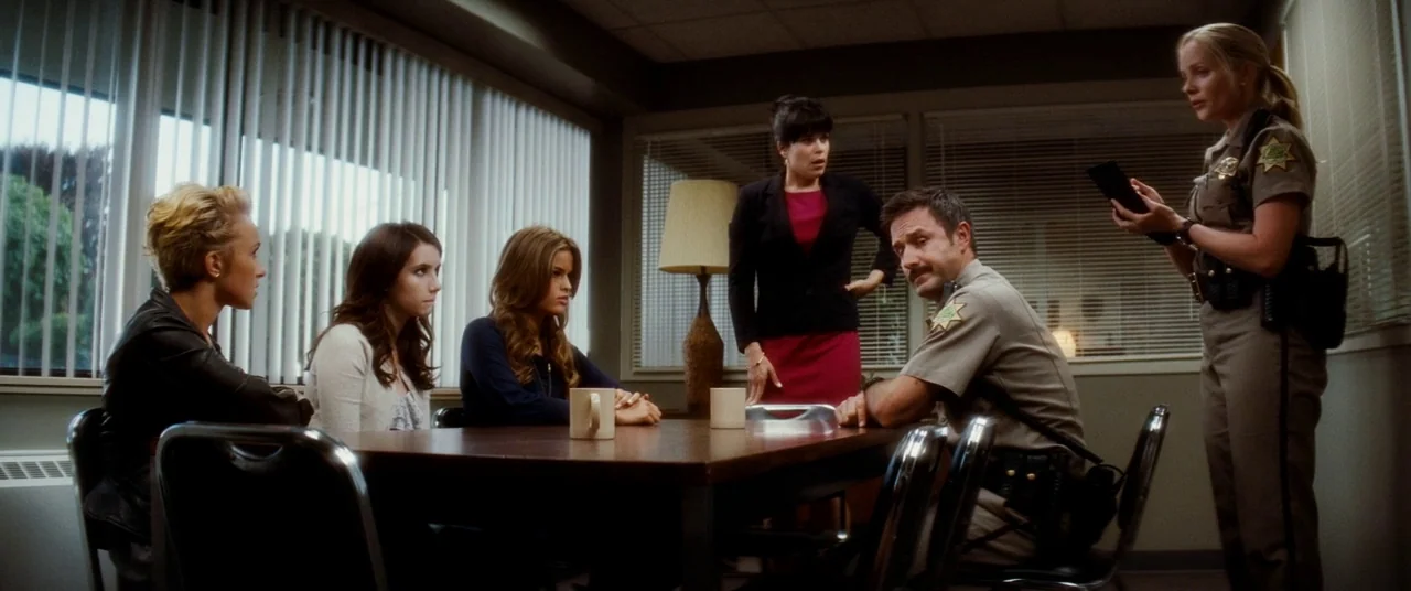 Scream 4 (2011) movie still: wide — A sterile room contains a wooden conference table surrounded by chairs and vertical blinds. People in police…