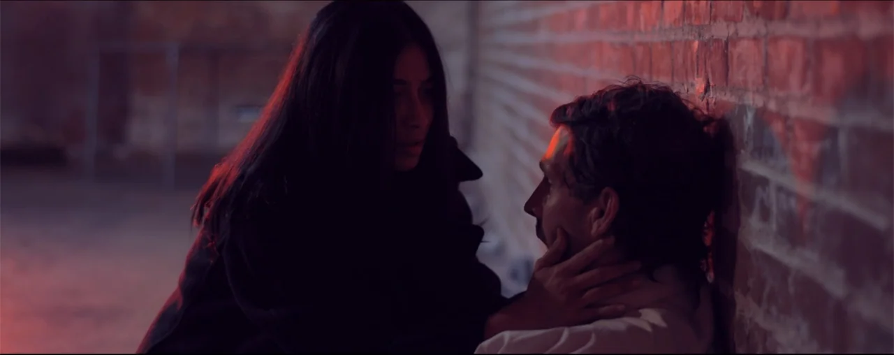 El Último Juego (2025) movie still: medium — An interior space with a rough brick wall illuminated by red neon lighting. A woman with dark hair…
