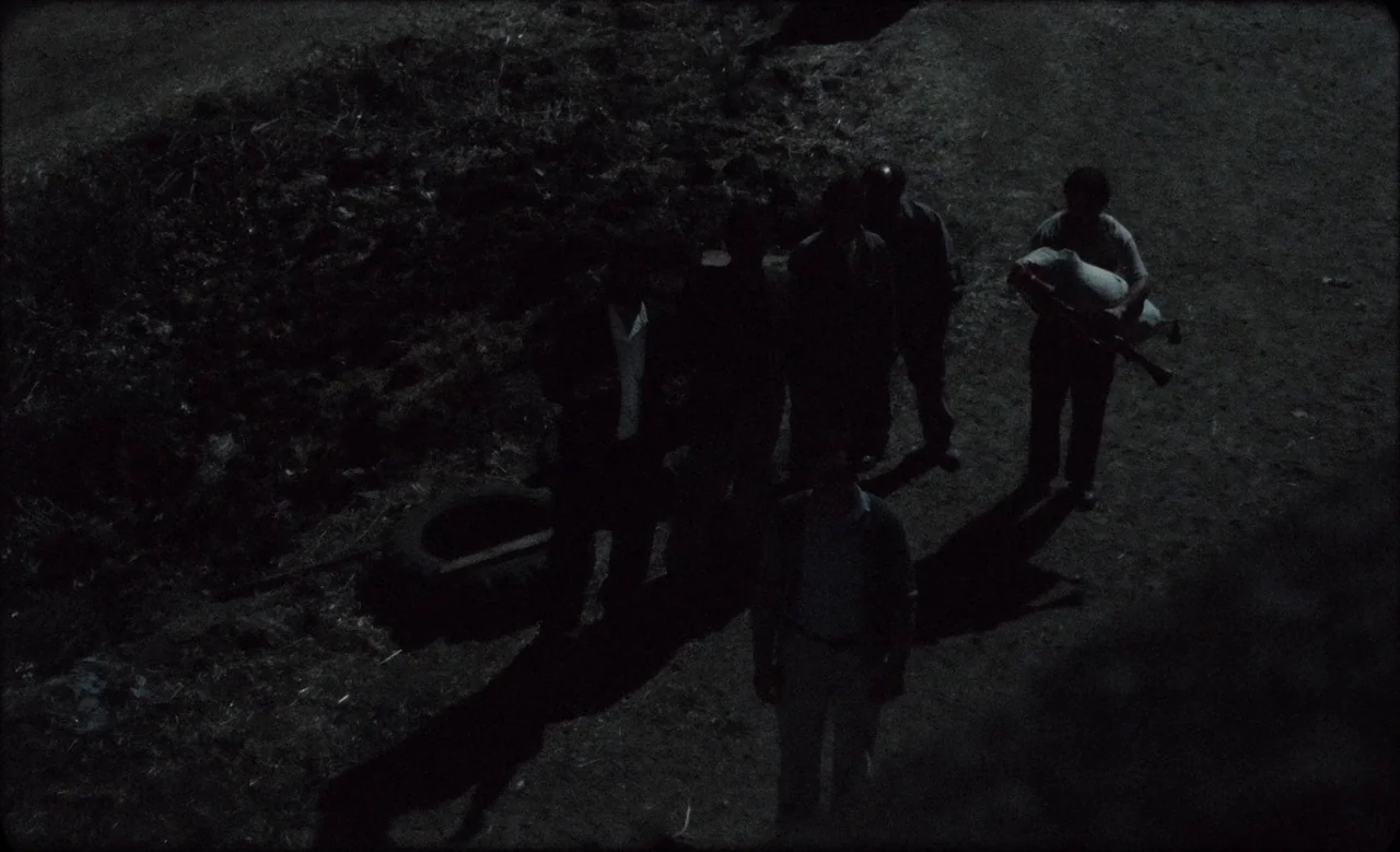 Happy as Lazzaro (2018) movie still: wide — A dark, unlit dirt lot is surrounded by uneven ground at night. Five men stand together while one man…