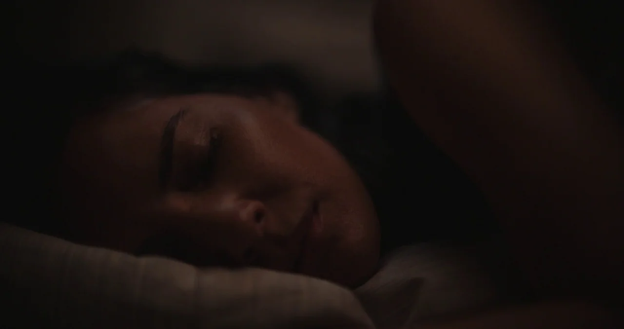 Violet (2021) (2021) movie still: closeup — A person sleeps in a darkened room, head resting on a soft pillow. Only the side of the face is…