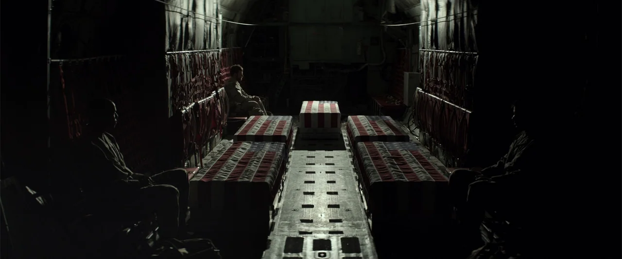 American Sniper (2014) movie still: wide — A dark military transport plane cargo hold contains several coffins draped in American flags. Three…