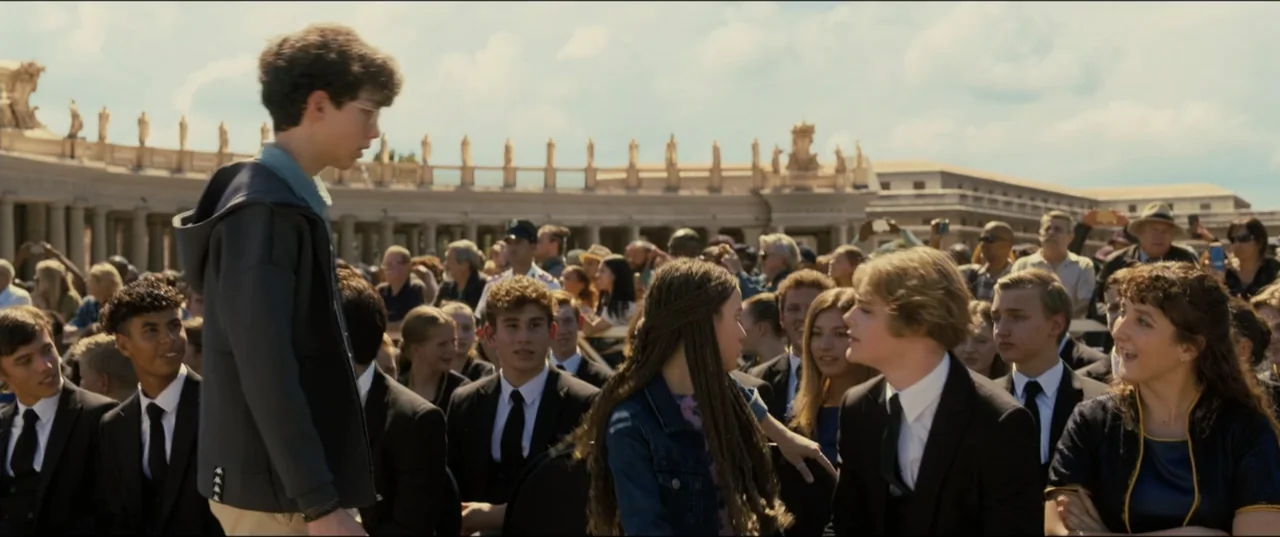 My Spy The Eternal City (2024) movie still: medium — A crowd of people in formal attire sits in a large open outdoor plaza. Two teenagers are…