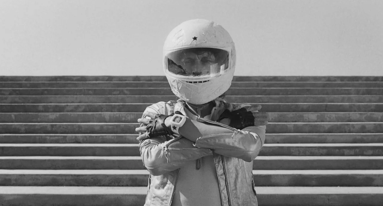 The Legend Of Kaspar Hauser (2012) movie still: medium — A set of concrete outdoor stairs rises in the background under bright daylight. A person in…
