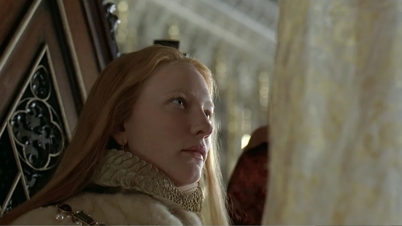 Elizabeth (1998) movie still: closeup — An opulent room features ornate dark wood paneling with intricate gothic carvings and molding. A young woman…