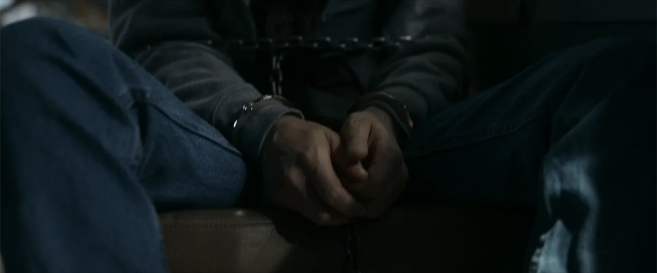 Flight Risk (2025) movie still: closeup — A dark vehicle interior with leather seating and minimal ambient light. A person's hands are clasped…