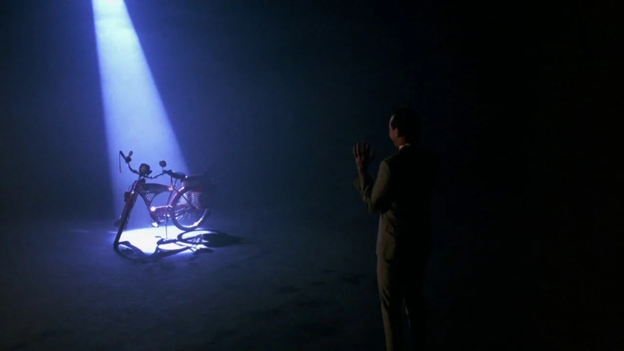 Pee-Wee’s Big Adventure (1985) movie still: wide — A dark, empty soundstage interior with a singular spotlight beam hitting a floor area. A man in a…