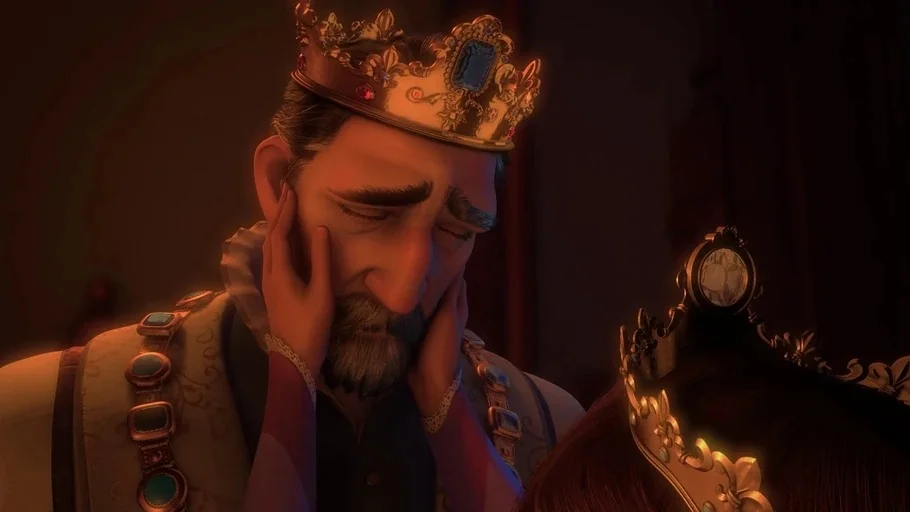 Tangled (2010) movie still: closeup — A dimly lit royal chamber features a king wearing an ornate crown. A woman rests her hands on the king's face…