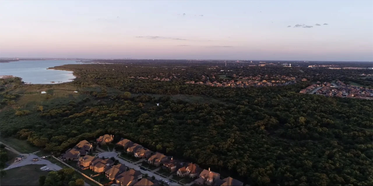 A Radical Life (2022) movie still: establishing — An aerial view shows a sprawling residential subdivision integrated into a dense forest landscape.…