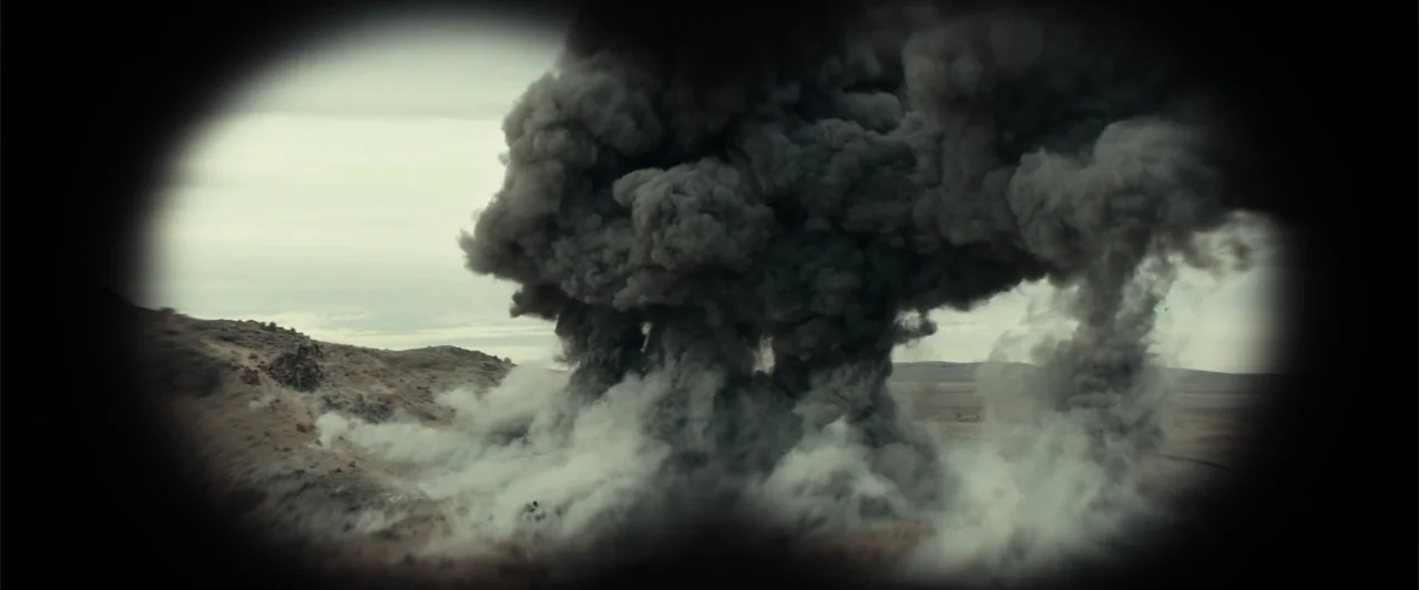 12 Strong (2018) movie still: wide — A vast, barren desert landscape is dominated by a massive, thick pillar of black smoke. The frame is viewed…