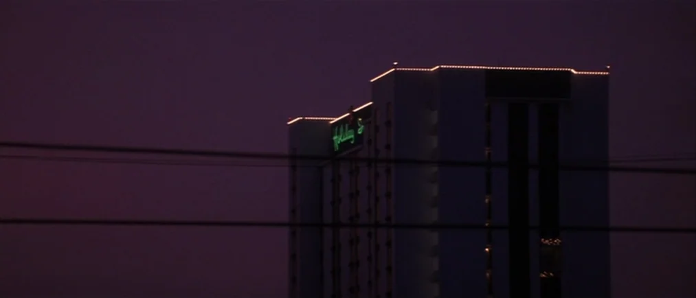 Donnie Darko movie still: establishing — A tall hotel building stands silhouetted against a deep purple twilight sky. Power lines cut horizontally…