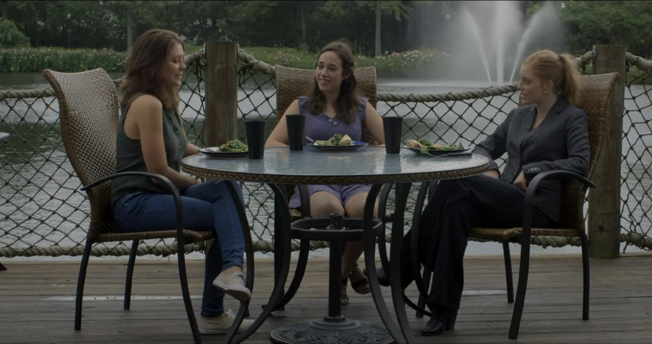 Faith, Love & Chocolate (2018) movie still: medium — A wooden deck overlooks a pond featuring a prominent water fountain in the distance. Three…