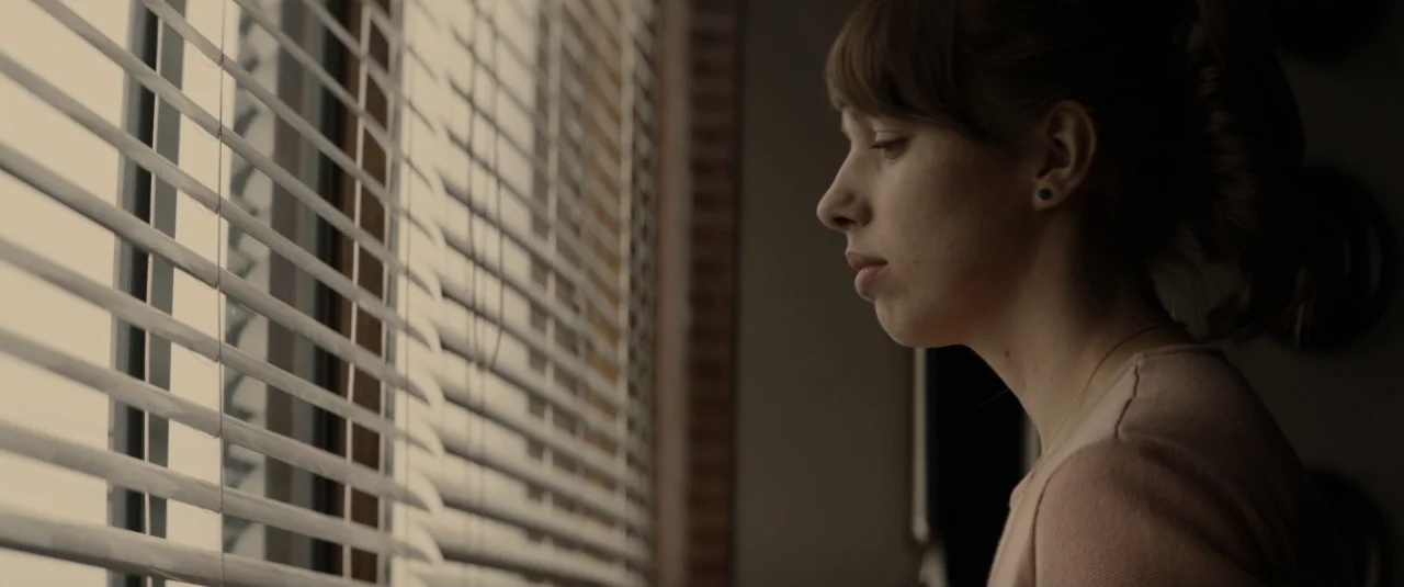 The Hole in the Ground (2019) movie still: closeup — A light-filled space with a large window covered by horizontal plastic blinds. A young woman…