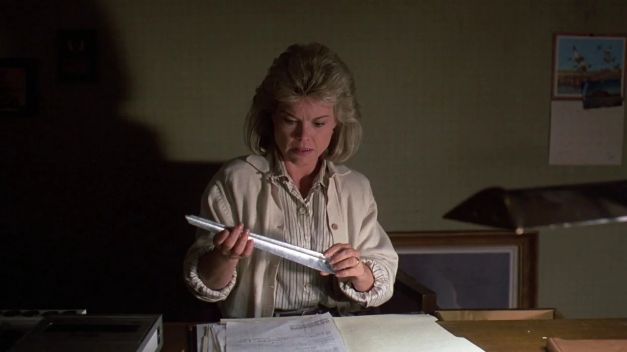 Friday the 13th Part VII: The New Blood (1988) movie still: medium — A dimly lit room with plain walls and a cluttered desk surface. A woman in a…