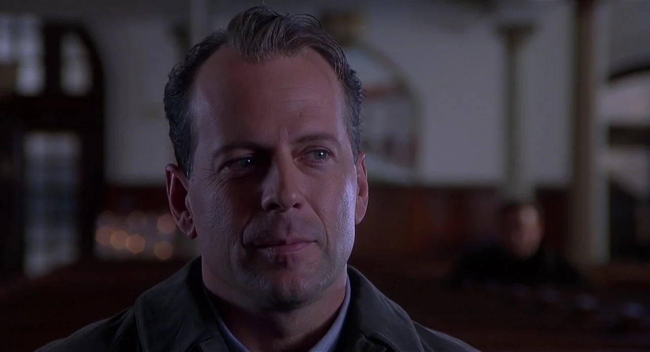 The Sixth Sense (1999) movie still: closeup — A dimly lit church interior with blurred wooden pews in the background. A man sits in the foreground…