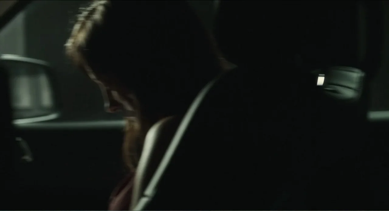 Haunter (2013) movie still: closeup — A dark car interior at night with limited ambient light filling the cabin. A woman sits with her head bowed…