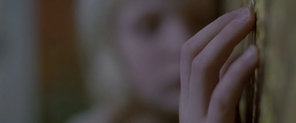 Let The Right One In (2008) movie still: closeup — A close-up captures a hand resting against a textured, light brown patterned wall surface. In the…